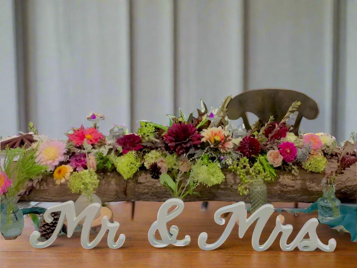 custom log vessel on wedding head table with flowers placed in it with Mr. and Mrs. wooden labels stating "mr." and "mrs." 